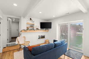 Living area featuring beam ceiling, light wood-style flooring, a glass covered fireplace, and recessed lighting