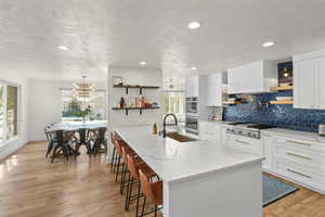 Kitchen featuring open shelves, white cabinets, light stone counters, plenty of natural light, and a textured ceiling