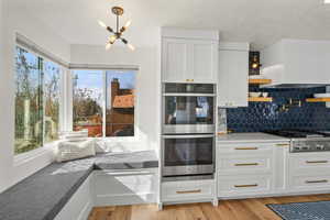Kitchen featuring stainless steel appliances, white cabinets, light stone counters, and light wood-style floors