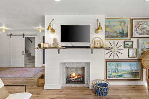 Living area with a barn door, wood finished floors, and a fireplace