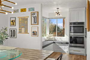 Kitchen featuring stainless steel double oven, a chandelier, white cabinets, and light wood-type flooring