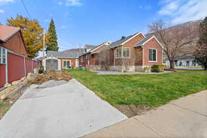 View of front facade featuring brick siding, a front yard, and a shed