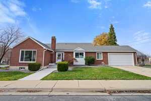 Ranch-style house featuring brick siding, a front lawn, concrete driveway, a chimney, and an attached garage