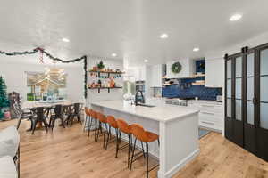 Kitchen with open shelves, white cabinets, a breakfast bar, backsplash, and light stone countertops