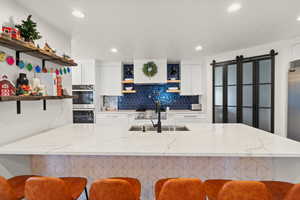 Kitchen with open shelves, white cabinetry, a kitchen breakfast bar, light stone counters, and appliances with stainless steel finishes