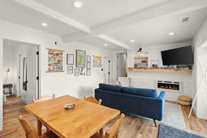Dining room with light wood finished floors, recessed lighting, beamed ceiling, and a glass covered fireplace
