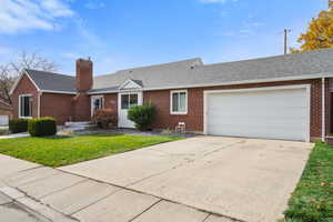 Single story home with a shingled roof, a front lawn, brick siding, concrete driveway, and a chimney