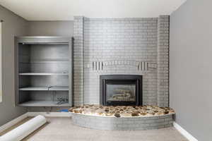 Detailed view of a brick fireplace, carpet flooring, and a textured ceiling