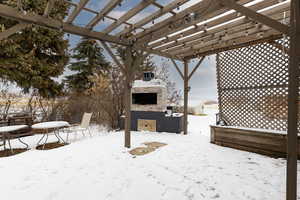 Yard layered in snow featuring an outdoor stone fireplace, a pergola, and a patio