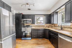 Kitchen with stainless steel appliances, light wood-type flooring, plenty of natural light, light stone countertops, and a textured ceiling