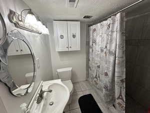 Bathroom featuring a textured ceiling, a tile shower, and light tile patterned floors