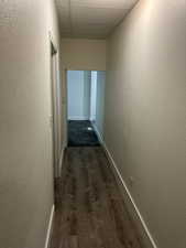 Hall featuring a textured wall, dark wood-type flooring, and a paneled ceiling