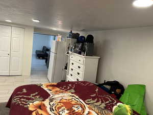 Bedroom with freestanding refrigerator, a textured ceiling, a closet, and light wood-style flooring