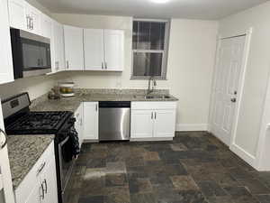 Kitchen featuring stainless steel appliances, stone finish floors, white cabinetry, and light stone counters