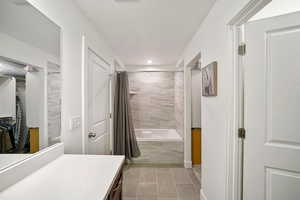 Bathroom with tiled shower / bath combo, vanity, a walk in closet, a textured ceiling, and light tile patterned floors
