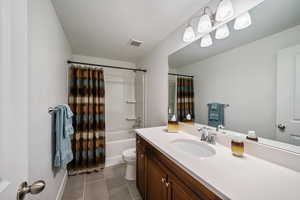 Bathroom with shower / bath combo with shower curtain, dark tile patterned flooring, vanity, and a textured ceiling