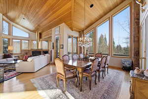 Dining room with wooden ceiling, a chandelier, light wood-style floors, high vaulted ceiling, and a fireplace