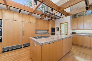 Kitchen with light wood-style flooring, an island with sink, paneled built in fridge, light stone countertops, and stainless steel electric stovetop
