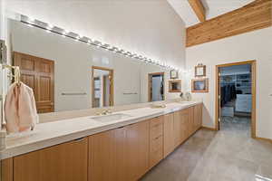 Full bathroom featuring double vanity, light carpet, a walk in closet, beam ceiling, and high vaulted ceiling