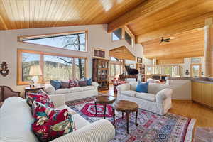 Living room with high vaulted ceiling, a wooden ceiling with exposed beams, light wood finished floors, and ceiling fan