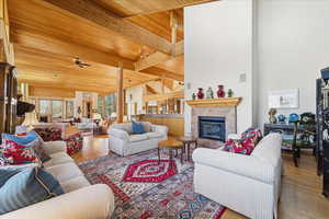 Living area with a ceiling fan, wood finished floors, a tiled fireplace, a wooden ceiling with exposed beams, and a high ceiling