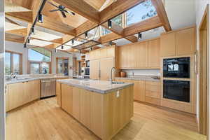 Kitchen with light brown cabinets, a kitchen island with sink, modern cabinets, light wood-style flooring, and stainless steel dishwasher