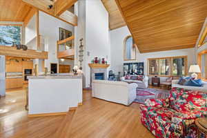 Living area with a tiled fireplace, high vaulted ceiling, wooden ceiling, and light wood-style floors