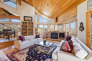 Living room with high vaulted ceiling, plenty of natural light, a glass covered fireplace, wood finished floors, and wood ceiling