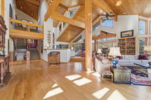 Living room with wood ceiling, high vaulted ceiling, light wood finished floors, stairs, and a ceiling fan