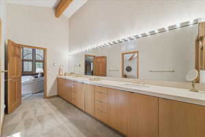 Full bathroom with light colored carpet, double vanity, a garden tub, high vaulted ceiling, and beamed ceiling