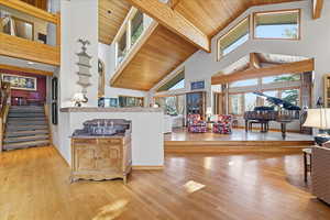 High vaulted ceiling, light wood-type flooring, a wooden ceiling with exposed beams, and open floor plan
