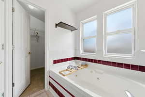 Primary Bathroom featuring a jetted tub, light tile patterned flooring, light carpet, and a spacious closet