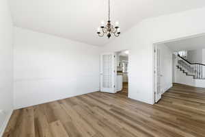 Unfurnished formal dining area featuring French doors, a chandelier, wood finished floors, lofted ceiling, and stairway