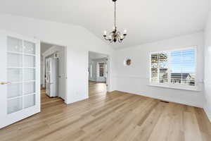 Unfurnished formal dining area featuring a chandelier, light wood-type flooring, and lofted ceiling