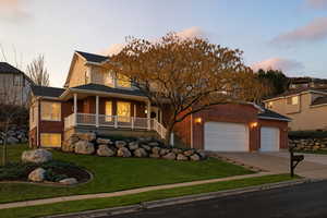 Twilight View, of front of house featuring a porch, a yard, driveway, brick siding, and an attached garage