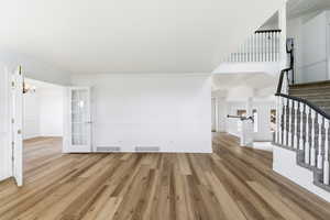 Unfurnished living room featuring wood finished floors, stairs, a chandelier, and crown molding