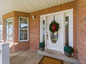 View of exterior entry featuring covered porch and brick siding