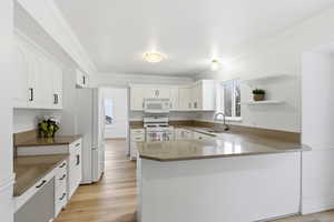 Kitchen with solid surface countertops, open shelves, a peninsula, white appliances, and white cabinets