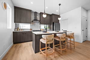 Kitchen featuring modern cabinets, a kitchen bar, an island with sink, wall chimney exhaust hood, and freestanding refrigerator