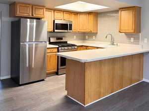 Kitchen with light countertops, updated stainless steel appliances, decorative backsplash, a peninsula, and light wood-type flooring