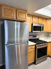 Kitchen featuring stainless steel appliances, tasteful backsplash, a textured ceiling, brown cabinets, and light stone countertops