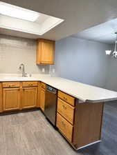 Kitchen with brown cabinets, a peninsula, light countertops, dishwasher, and a textured ceiling