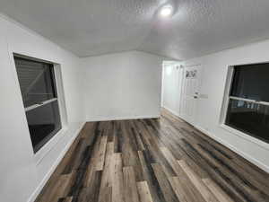 Spare room featuring dark wood-type flooring, vaulted ceiling, a textured ceiling, and a decorative wall