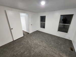 Unfurnished room with a textured ceiling and dark carpet