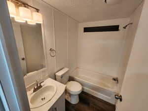 Bathroom featuring a decorative wall, a textured ceiling, vanity, bathing tub / shower combination, and dark wood-type flooring