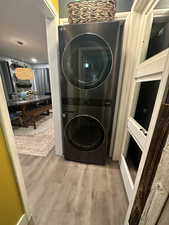 Washroom with stacked washer / drying machine and light wood-style floors