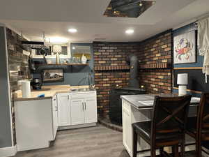 Kitchen featuring open shelves, white cabinetry, light wood-style flooring, a wood stove, and brick wall