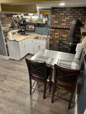 Kitchen featuring white cabinetry, a wood stove, light countertops, light wood-type flooring, and brick wall