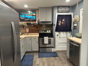 Kitchen featuring butcher block counters, stainless steel appliances, gray cabinetry, dark wood finished floors, and recessed lighting