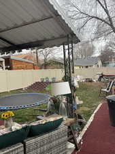 Fenced backyard featuring a trampoline and a patio
